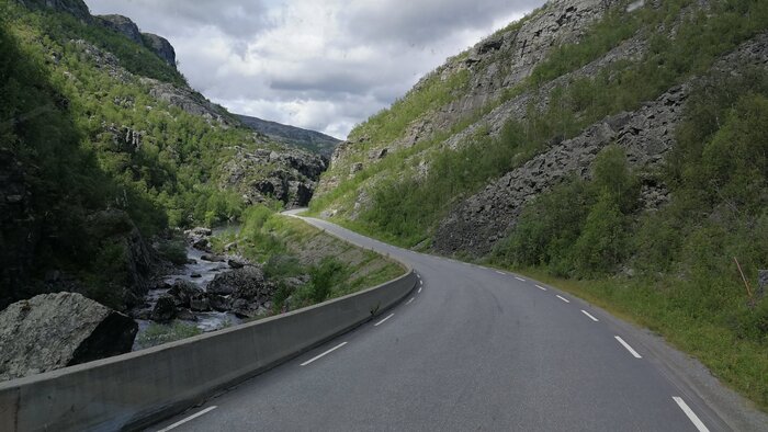 Eine kurvenreiche Straße durch eine felsige Gebirgslandschaft mit einem Bach und grünen Hängen. Foto: Elke Ahre Eine kurvenreiche Straße durch eine felsige Gebirgslandschaft mit einem Bach und grünen Hängen. Foto: Elke Ahrer